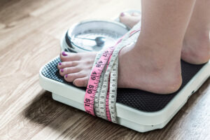 Woman weighed on weighing scale tied up with tape measure